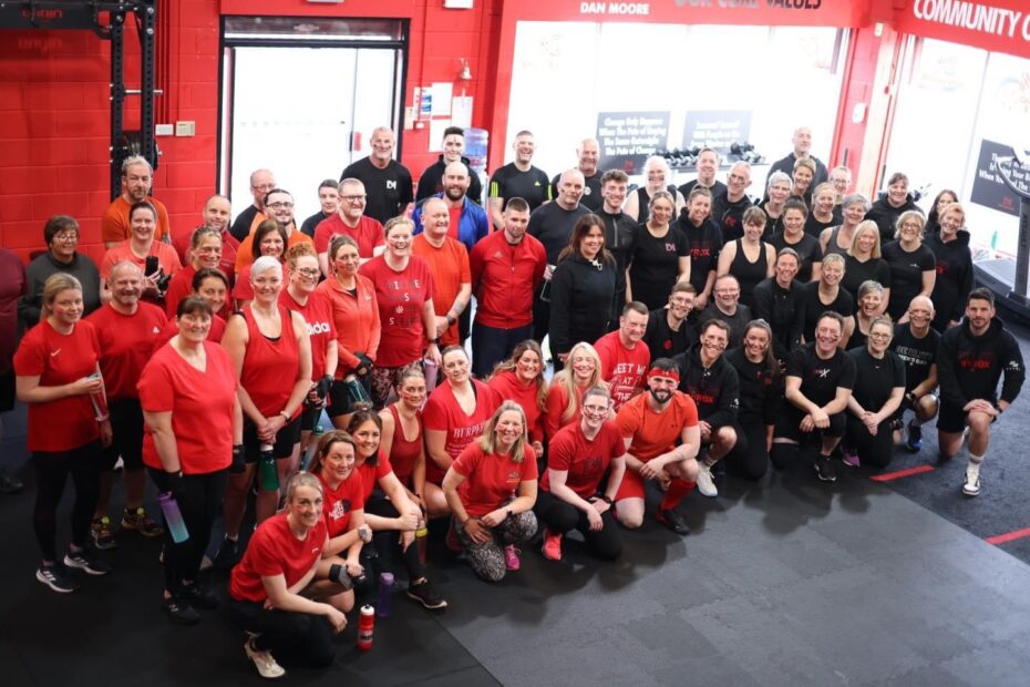 A large community of people dressed in black and red gym clothes pose for a picture in the DM Elite gym